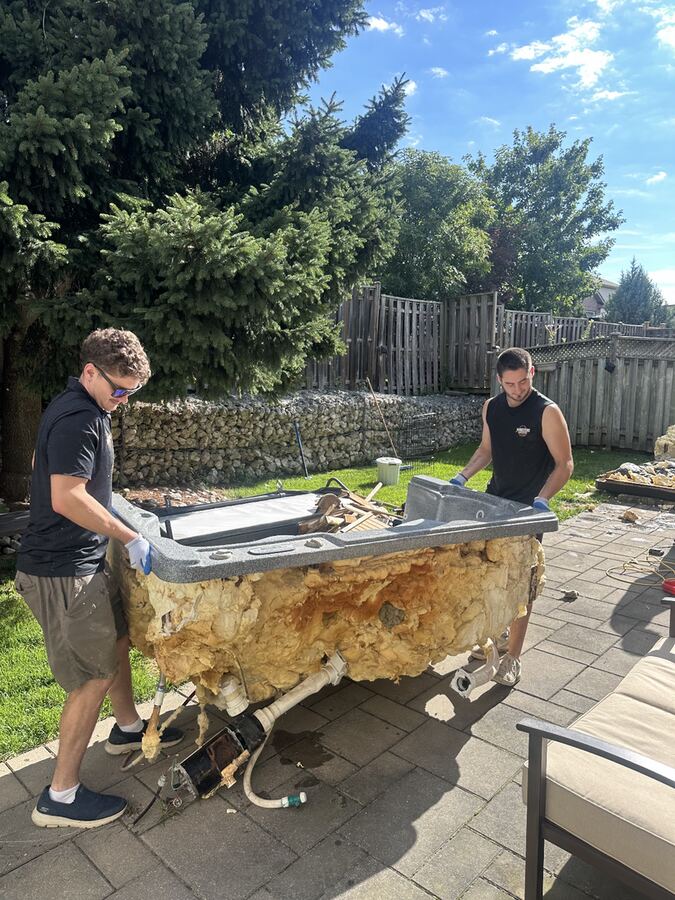 Two Youngsters crew members lifting a gutted hot tub off a backyard patio